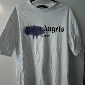 Palm angels tshirt - Vit t-shirt från Palm Angels med svart och lila tryck på bröstet där det står 'Palm Angels London'. Klassisk passform med lite oversized fit. Storlek M.
