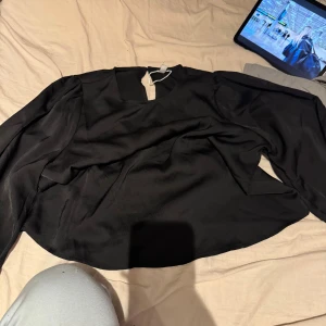 Svart blus från Only med vida ärmar - Säljer en svart blus från Only i storlek M. Blusen har vida, långa ärmar med resår vid ärmslut och en lätt glansig finish. Perfekt för dig som gillar en stilren och trendig look. Snyggt fall och rund halsringning.