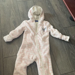 Mycket fin baby fleeceoverall - Jätte söt fleeceoverall storlek 62/68. Märket på overallen är Lupilu.Luvan har små söta öron, overallen är rosa/vit. Finns vantar, strumpor som är påsydda som man kan vika över hand/ fötter. Mycket fint skick. 