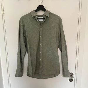 Grön linneskjorta från Selected Homme - Snygg grön skjorta i linne från Selected Homme. Skjortan har klassisk krage, knäppning framtill med vita knappar och långa ärmar med manschett. Perfekt för en chill och stilren look.