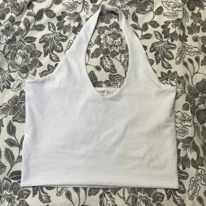 Vit halterneck linnetopp Stradivarius - Säljer en vit halterneck linnetopp från Stradivarius i storlek S. Toppen har djup urringning och är ärmlös, perfekt för varma dagar. Tillverkad i mjuk bomull som känns skön mot huden. Enkel och stilren design som är lätt att matcha med olika outfits.