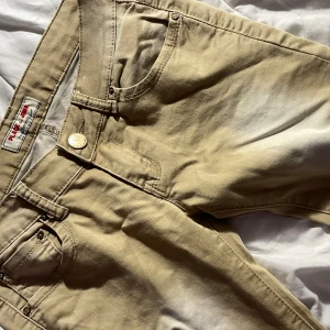 Beige skinny jeans - Snygga beige skinny jeans från Place Du Jour med klassiska fem fickor och guldfärgade detaljer. Byxorna är tillverkade i mjuk bomull med lite stretch för extra komfort. Perfekta för dig som gillar en slimmad passform och stilren look.