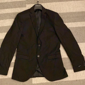 Svart kostym från Jack & Jones  storlek 46 SLIM FIT - Säljer en klassisk svart kostym från Jack & Jones. Kavajen har två knappar, smal krage och fickor med lock. Byxorna är raka och har pressveck. Perfekt för dig som vill ha en stilren och tidlös look. Materialet är mjukt och följsamt.