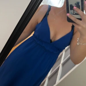 Blå långklänning med v-ringning - Säljer en snygg blå långklänning med djup v-ringning och smala axelband. Klänningen har en markerad midja och ett flowy fall som ger en elegant siluett. Perfekt för dig som vill sticka ut med en färgstark look.