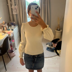Vit ribbad långärmad topp - Säljer en vit ribbad topp med långa puffärmar och rund halsringning. Toppen har en feminin och stilren look med diskreta rynkdetaljer vid ärmsluten. Perfekt att styla med jeans eller kjol för en fräsch outfit.