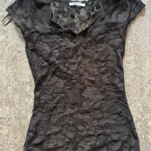Svart spetströja  - Supersnygg tröja från Gina Tricot i genombruten spets med blommigt mönster. Tröjan har korta ärmar och en figurnära passform som framhäver siluetten. Perfekt för dig som vill sticka ut med en elegant och trendig look.