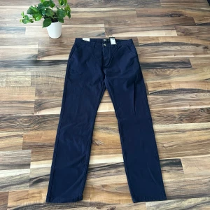 Mörkblå chinos från 157, stl S - Snygga mörkblå chinos från 157 i modellen Grim. Byxorna har raka ben, klassiska fickor och bälteshällor. Perfekta för dig som gillar en clean och stilren look. Tillverkade i mjukt bomullsmaterial som känns skönt mot huden.