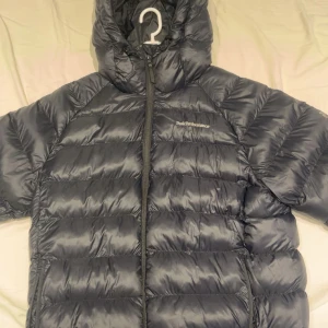 Svart dunjacka Peak Performance L men passar även M - Säljer en svart dunjacka från Peak Performance i storlek L. Jackan har huva, quiltad design och dragkedja framtill. Perfekt för kalla dagar och har en clean look med diskret logga på bröstet. Modellen är W Tomic Insulated Hood. Nypris ligger ungefär på 2100