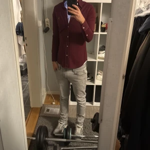 Vinröd skjorta från Ralph Lauren - Säljer en vinröd långärmad skjorta från Ralph Lauren med klassisk krage och knappar framtill. Skjortan har broderad logga på bröstet och är i bomullsmaterial. Passformen är slim och skjortan har en stilren look som passar perfekt till jeans. Sitter lite tajt på mig som är 170