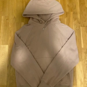 Rosa hoodie från AMI Paris - Säljer en rosa hoodie från AMI Paris med broderad logga på bröstet och diskret AMI-detalj vid fickan. Tröjan har huva med snörning och är tillverkad i mjuk bomull. Perfekt för chill dagar och snygg till jeans eller joggers.