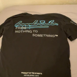 Svart t-shirt från Hoodrich - Svart t-shirt med tryck i blått och vitt på ryggen. Kortärmad modell med streetwear-vibe och coolt grafiskt tryck. Från Hoodrich, STRI L