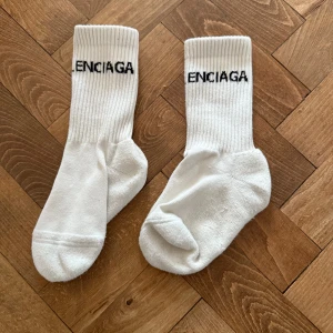 Vita ribbade Balenciaga strumpor strl 35-39 - Säljer ett par vita ribbade strumpor från Balenciaga med svart broderad logga upptill. Strumporna är i klassisk modell med mjuk insida och stretchig passform. 