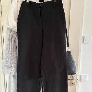 Svarta kostymbyxor med raka ben - Stilrena svarta kostymbyxor med raka, lite vidare ben och klassisk midja. Byxorna har hällor för bälte, diskreta bakfickor. Perfekta för en clean och dressad look. använda 1gång. säljes då dom ej passar