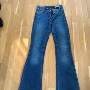 Blå bootcut jeans från Vero Moda - Snygga blå jeans från Vero Moda med bootcut-modell och klassisk femficksdesign. Jeansen har hög midja och är tillverkade i ett mjukt denimtyg som sitter skönt. Perfekta för dig som gillar en retroinspirerad look med utsvängda ben.