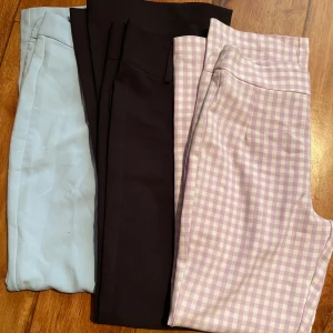 Tre par kostymbyxor  - Säljer tre par byxor: ett par ljusblå med smal passform, ett par svarta bootcut-byxor och ett par lila-vita rutiga byxor med smal passform. Perfekta för dig som gillar stilrena och trendiga färger. Alla har klassisk midja och är i mjukt material. Dom svarta är köpta på Gina Tricot och dom färgade på Bik Bok. Köpare står för frakt.