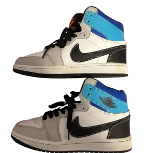 Nike Air Jordan 1 High blå/vit/svart - Säljer ett par Nike Air Jordan 1 High i storlek 37. Skorna har en snygg färgkombo med blå, vit och svart, klassisk svart swoosh och svarta skosnören. Ovandelen är i skinn med perforerad tå och högt skaft. Perfekta för dig som vill sticka ut med en ikonisk sneaker.