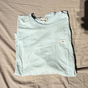 Ljusblå långärmad tröja Acne Studios - Ljusblå långärmad tröja från Acne Studios med klassisk rund hals och det ikoniska Face-logotypen på bröstet. Tillverkad i mjuk bomull som känns skön mot huden. Perfekt för dig som gillar stilrena och minimalistiska plagg.