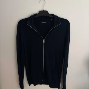 Mörkblå hel zip - Mörkblå hel zip tröja från Jack & Jones med hel dragkedja framtill och hög krage. Storlek: S - Skicket på tröjan är väldigt bra utan några defekter alls - Pris: 250 - Nypris: 499 - Skriv vid funderingar!