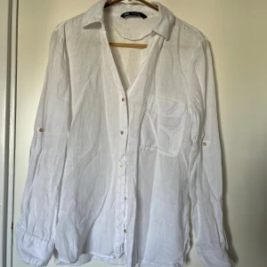 Vit linneskjorta från Zara  - Säljer en fin vit skjorta från Zara i 100% linne. Skjortan har klassisk krage, bröstficka, knappar framtill och långa ärmar med knappdetaljer, kan vikas upp och knäppas på ärmarna för trekvartsärmar. Perfekt på varmare dagar. Använd ett par gånger, fint skick. 