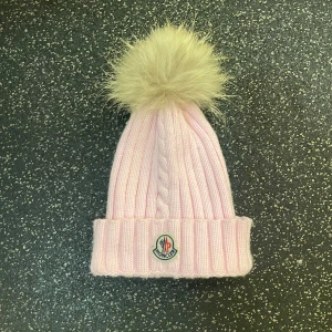 Ljusrosa Moncler mössa med pälsboll - Superfin ljusrosa ribbstickad mössa från Moncler med stor fluffig pälsboll på toppen. Mössan har uppvikt kant och klassisk Moncler-logga framtill. Perfekt accessoar för kalla dagar och ger en söt touch till din vinterstil. Säljs för att min syrra inte använder den längre. Nyskick då den knappt är använd skick då den knappt har använts. Nypris ca 3800 den är ganska liten i storleken