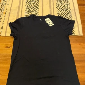 Svart t-shirt från C XS - En basic svart t-shirt från Cubus i storlek XS. T-shirten har rund halsringning och korta ärmar. Tillverkad i mjuk bomull, perfekt för en clean och enkel stil. Passformen är normal och materialet känns skönt mot huden.