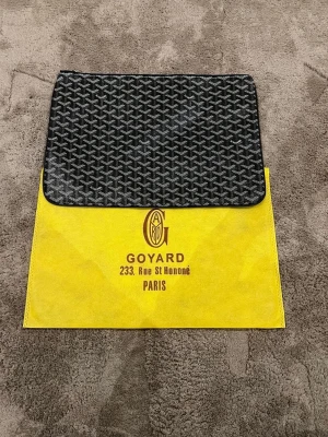 Svart kuvertväska  - Snygg svart kuvertväska med det klassiska -mönstret i vitt och grått. Väskan är rektangulär och har dragkedja upptill. Tillverkad i canvas med läderdetaljer. Levereras med original gul dustbag med logga. Skriv innan köp