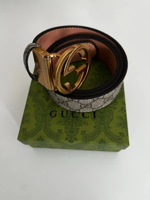 GG  bälte guldspänne - Säljer ett GG Supreme bälte med klassiskt monogrammönster i beige och brunt. Bältet har ett stort, rundat spänne i guld med GG-logga och insida i ljust läder. Perfekt för att lyfta vilken outfit som helst. Om ni funderingar eller frågor skriv till mig