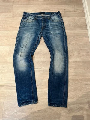 Scotch&soda jeans med slitningar - Snygga blå jeans från Replay med tydliga slitningar och ljusare partier framtill och baktill. Klassisk femficksmodell med slim ben och normal passform. Jeansen har en cool tvättad look och är tillverkade i bomull.