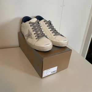 Golden goose - Snygga vita sneakers med grå snörning och grå stjärndetalj på sidan. Skorna har en klassisk låg profil och platt sula. Perfekta för dig som gillar stilrena och moderna sneakers.