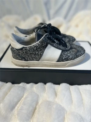 Valentino flycrew glittriga sneakers - Snygga sneakers från Valentino Garavani med svart och vitt glittrigt mönster, svarta snören och vit panel på sidan. Skorna har rund tå och platt sula, perfekta för dig som vill sticka ut med stil. Klassisk low-top modell. Säljs inte längre. Strl 36