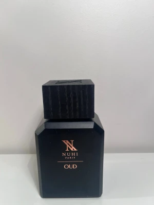 NUHI Paris Oud parfym - Snygg mansparfym från NUHI Paris med doften Oud. Flaskan är svart med en matt finish och har en stilren, fyrkantig form med guldiga detaljer på framsidan. Locket är också svart och har en robust, kantig design som ger en lyxig känsla. Endast använd på gånger