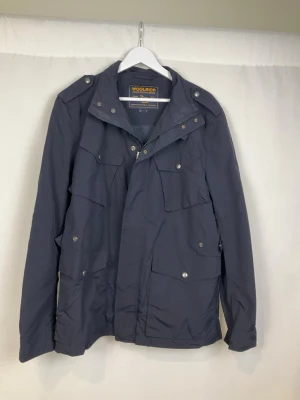 Woolrich Jacka - Tja säljer en snygg blå jacka från Woolrich med krage och detaljer som dragkedjor och knappar framtill. Jackan är i väldigt fint skick och säljs för endast 1399kr. Nypris över 6000kr. Skriv vid frågor eller ifall du vill ha fler bilder. Storlek Large.