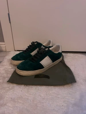 Valentino Garavani gröna sneakers mocka - Snygga gröna sneakers från Valentino Garavani i mjuk mocka med vita detaljer och svarta skosnören. Klassisk låg modell med rund tå och platt sula. Perfekta för dig som vill ha en stilren och exklusiv look. Skriv vid köp och frågor