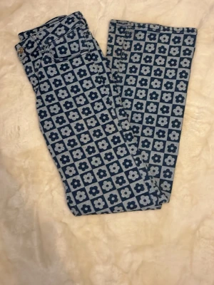 Blommiga bootcut jeans från H&M Divided - Snygga blå jeans från H&M Divided med unikt blommigt mönster i rutigt. Jeansen har klassisk femficksmodell och normal passform. Perfekta för dig som vill sticka ut med en cool retrostil. Materialet är klassisk denim.