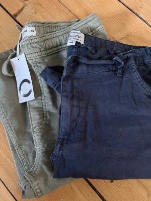Två par short i blått och grönt - Säljer två par short, ett par i mörkblått (använda i dtl 164) och ett par i olivgrönt (helt oanvända stl 158).Perfekta för både vardags och fint. 125kr för båda