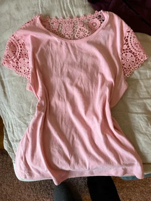 Rosa topp med spetsdetaljer - Söt ljusrosa topp med spets vid axlar och halsringning. T-shirten har korta ärmar och en rund hals, tillverkad i mjuk bomull. Perfekt för dig som gillar romantiska detaljer och en feminin stil. Köpt på vinted för nåt år sen men kommer inte längre till användning ❤️❤️❤️ tror att den förra ägaren hade köpt den utomlands