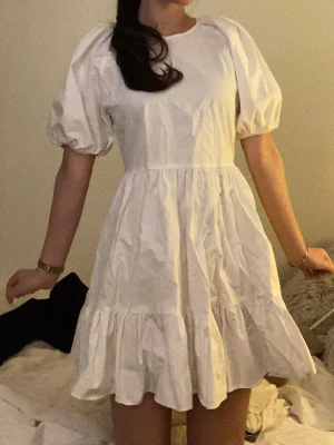 Studentklänning från NELLY🤍 - Säljer denna suuuupersöta klänningen med puffärmar och volangkant. Klänningen har öppen rygg med två gulliga rosetter som man knyter ihop och rund halsringning. Tillverkad i ett bomullstyg som känns luftigt och perfekt för varma dagar, student eller resa!✨            Från Nelly X Glamorous kollektion (endast använd 1-2 ggr)🙌