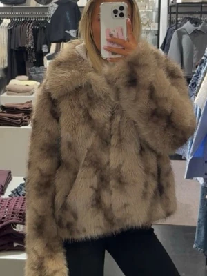 Beige fluffig pälsjacka från MbyM - Supermjuk och fluffig beige pälsjacka från Ivyrevel med mörkare inslag. Jackan har en klassisk krage och rak passform, perfekt för att hålla värmen under kyliga dagar. Stängs framtill och har en lyxig känsla tack vare det tjocka pälsmaterialet. Nypris 2500kr