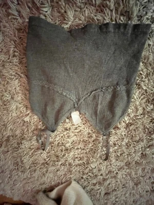 Grå ribbat linne med spetsdetaljer - Snyggt grått linne i ribbat material med spetsdetaljer längs bysten och justerbara axelband. Perfekt att styla under en skjorta eller kavaj. Mjuk och stretchig för en bekväm passform.