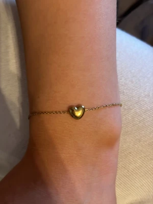 Guldarmband med hjärta från Edblad - Superfint guldarmband från Edblad med en tunn kedja och ett litet hjärta i mitten. Perfekt för dig som gillar stilrena och söta smycken. Justerbar längd med liten bricka vid låset. Säljer då det ej kommer till användning 