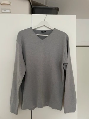 Grå stickad tröja från Sand Men - Snygg grå stickad tröja från Sand Men med V-ringning och långa ärmar. Tröjan har en enkel och stilren design som passar perfekt till olika outfits. Tillverkad i mjukt material för skön komfort.