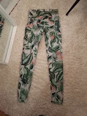 Mönstrade leggings från Cubus - Snygga leggings från Cubus med tropiskt bladmönster i grönt, vitt och inslag av rosa. Tight passform och medelhög midja, perfekta för träning med en liten minificka för nåt. Nästan aldrig använda och bra skick