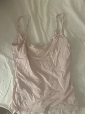 Ljusrosa linnetopp med smala band - Söt ljusrosa linnetopp med smala axelband och enkel design. Tillverkad i mjuk bomull som känns skön mot huden. Perfekt att styla lager på lager eller bära som den är under varma dagar.