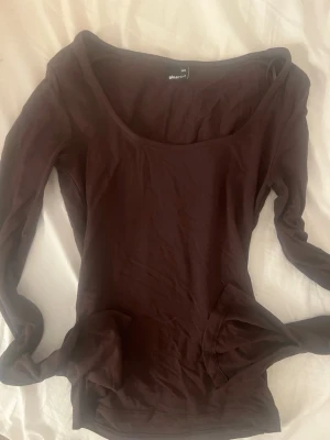 Mörkbrun långärmad topp från Gina Tricot - En enkel och stilren mörkbrun långärmad topp från Gina Tricot. Modellen har en djup, rundad ringning och är tillverkad i mjuk bomullsmix. Perfekt att styla med jeans eller kjol för en clean look.