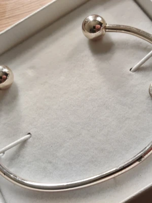 Kopparfärgat ish  armband från Isadora - Snyggt och stilrent armband i en ungefär kopparfärg i okänd metall från Isadora. Armbandet har en öppen design med två klotformade ändar och en liten rund bricka med Isadora-loggan. Perfekt för dig som gillar minimalistiska accessoarer. Aldrig använt men har någon typ av skada men som man inte lägger så mycket märke till. Självklart får man end boxen💕. 