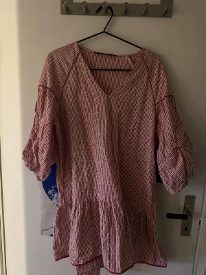 Rödvit randig volangklänning - Söt rödvit randig klänning med volangkant och v-ringning. Klänningen har trekvartsärm med lätt puff och avslappnad passform. Tillverkad i ett luftigt bomullstyg, perfekt för varma dagar. Lite kort på mig som är 168cm. Är i strl L men skulle säga mer M. KÖPAREN STÅR FÖR FRAKT