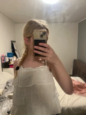 Vit volang-linnetopp med smala axelband - Supersöt vit linnetopp från H&M med flera lager volanger och smala axelband. Toppen är luftig och perfekt för varma dagar, med en lätt och flowy känsla. Enkel att matcha med jeans eller kjol för en fräsch look.