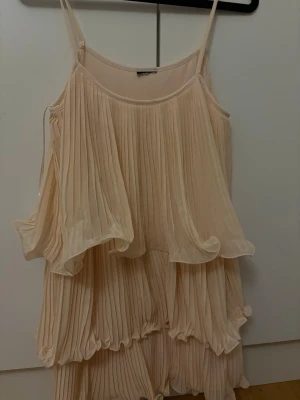 Plisserad rosa kortklänning - Säljer en superfin plisserad kortklänning i rosa med tunna axelband och volangdetaljer. Klänningen har ett luftigt och flowy fall, perfekt för varma dagar. Materialet känns lätt och svalt mot huden.