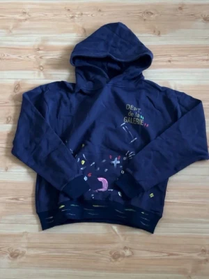 Mörkblå hoodie från Gallery Dept. - Snygg mörkblå hoodie från Gallery Dept. med trycket 'DÉPT. de la GALERIE' i gult på bröstet och färgglada grafiska detaljer framtill. Pris diskuteras vid mess innan köp viktig info sägs även då. Pris kan diskuteras vid smidig o snabb affär samt.