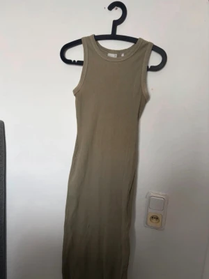 Beige ribbad långklänning Etirel - Säljer en beige ribbad långklänning från Etirel i storlek M. Klänningen är ärmlös och har en rund halsringning. Perfekt för en enkel och stilren look under varmare dagar. Obs! En del använd och lite urtvättad